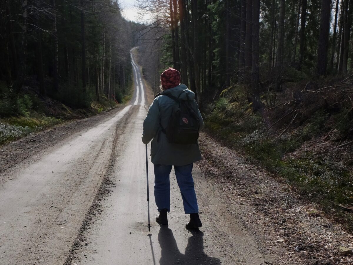 En friluftsklädd kvinna vandrar bort från kameran på en grusväg.