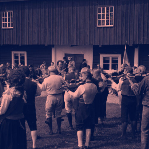 Spelmän spelar fiol inför publik framför Siggebohyttans bergsmansgård.